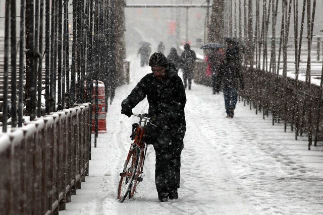 A man walks his bike over the Brooklyn Bridge during snow